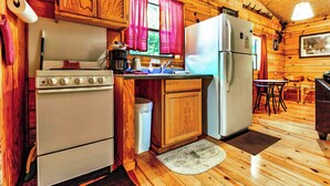 Une cuisine rustique aménagée dans une cabane en bois, avec un poêle, un évier, un réfrigérateur et des placards en bois.
