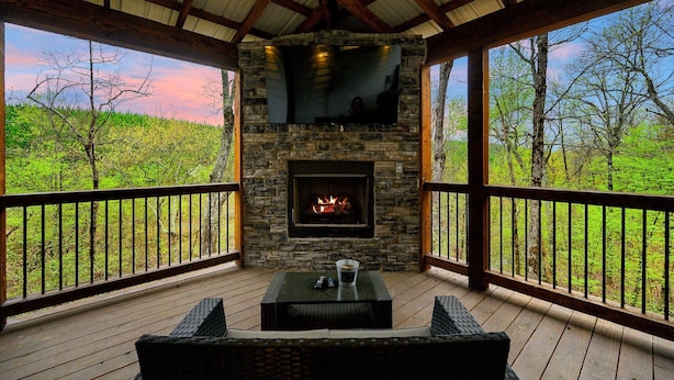 A covered outdoor area with a stone fireplace, wooden deck, and wicker furniture.