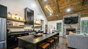 A modern kitchen with a central island, black cabinets, and a stone fireplace.