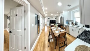Una cocina moderna con comedor, armarios blancos y un ventanal grande.