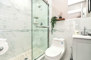 Een badkamer met een glazen douchecabine, toilet en een wastafel met spiegel.