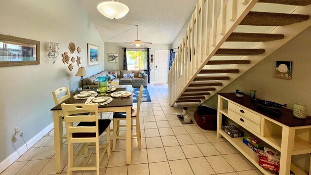 Comedor con mesa dispuesta para cuatro, sofá al fondo y una escalera de madera.