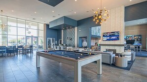 Un área de piscina interior moderna con mesa de billar, asientos y una pantalla de televisión.