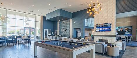 A modern indoor pool area with a pool table, seating, and a TV screen.