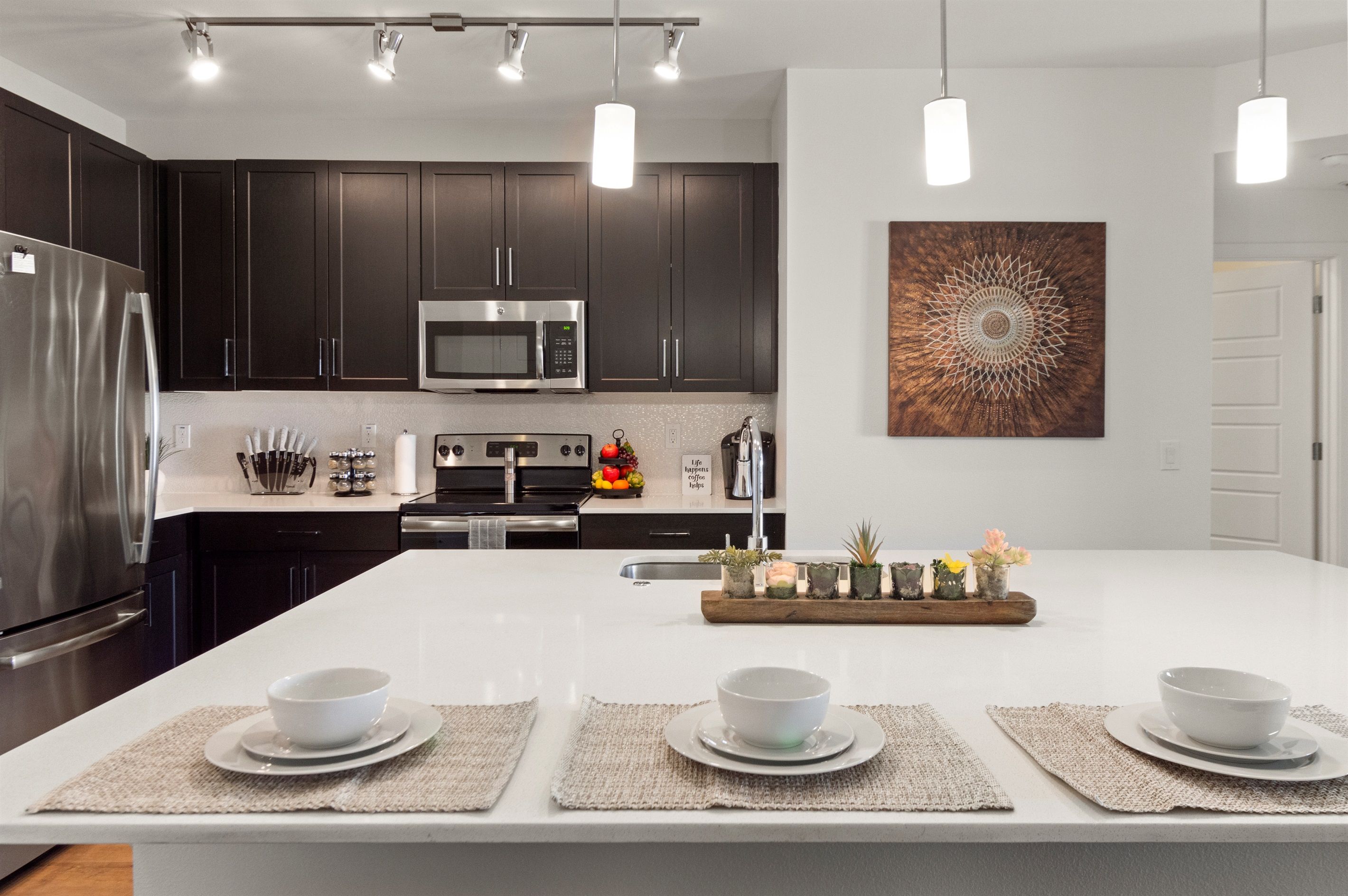 Una cocina moderna con armarios oscuros, electrodomésticos de acero inoxidable y una isla central con cuencos y manteles.
