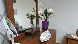 A wooden vanity with a mirror, a white vanity lamp, a purple vase with white flowers, and a decorative glass piece on a wooden dresser. - Casa Laranjeira in the historic city (Faro)