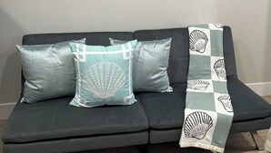 A dark grey sofa with three decorative pillows and a beach-themed throw blanket.