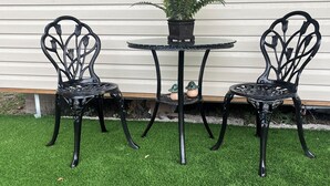 A small outdoor seating area with two black metal chairs and a round table, surrounded by artificial green grass.