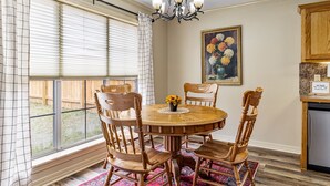 A dining area with a round wooden table, four wooden chairs, a chandelier, a painting of flowers, and a kitchen area with wooden cabinets. - Charming house minutes from everything in Monroe/West Monroe! 5-Star hosts! (West Monroe)