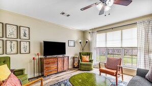 A living room with a flat-screen TV, green armchairs, a sofa, and a ceiling fan. - Charming house minutes from everything in Monroe/West Monroe! 5-Star hosts! (West Monroe)