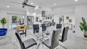 Una cocina moderna con armarios blancos, un refrigerador de acero inoxidable y un comedor con mesa de vidrio y sillas negras.