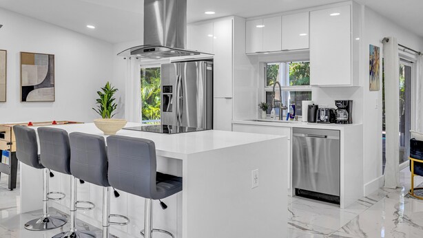 Una cocina moderna con armarios blancos, electrodomésticos de acero inoxidable y una isla central con taburetes de bar.