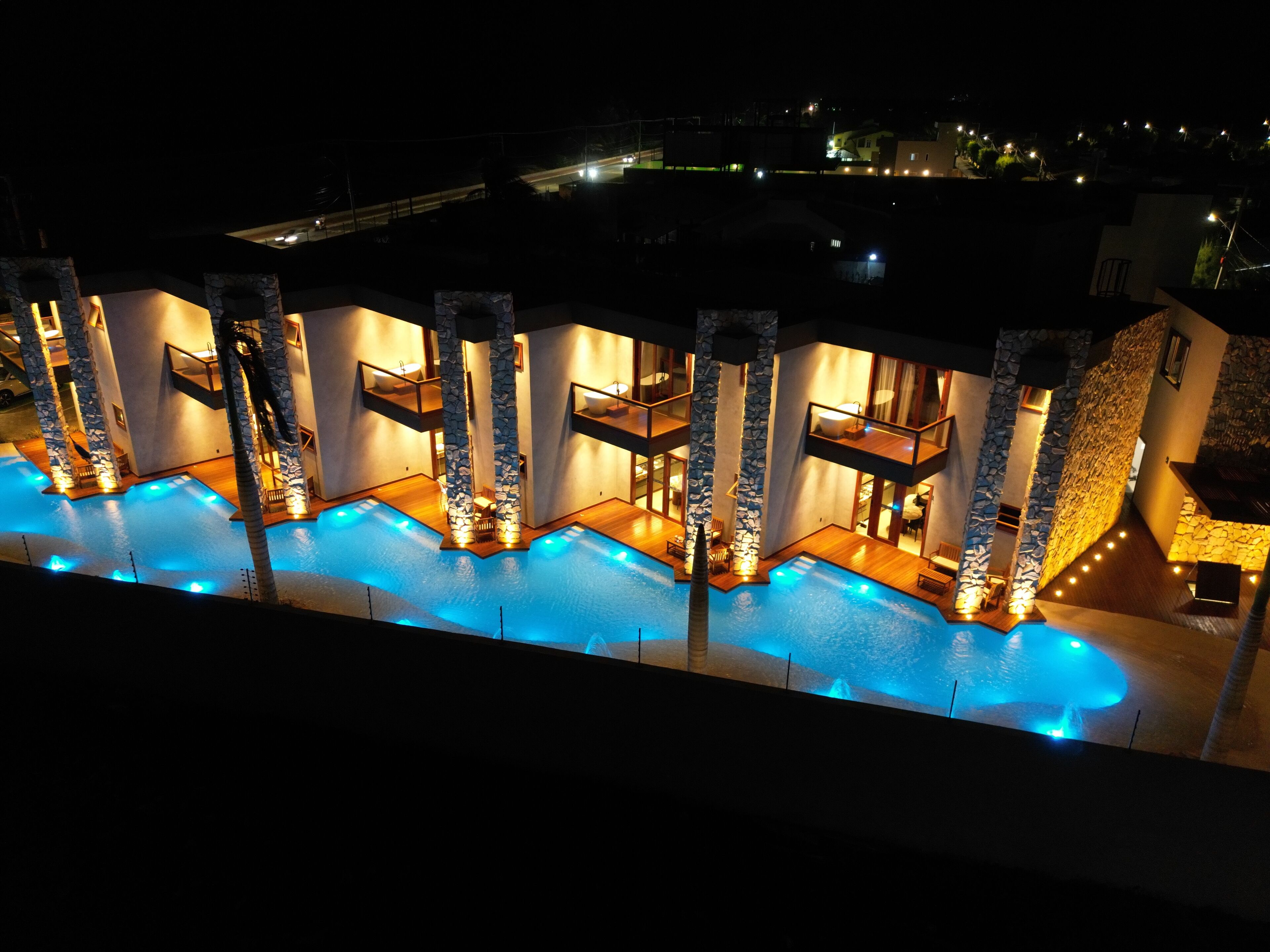 Un área de piscina con varios niveles, pilares de piedra, múltiples balcones y ambiente nocturno.