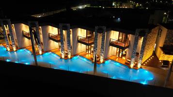 Un área de piscina con varios niveles, pilares de piedra, múltiples balcones y ambiente nocturno.