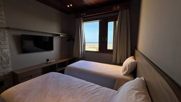 A hotel room with two beds, a TV mounted on the wall, and a window with a view of the beach.