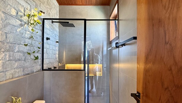 A modern bathroom with a stone wall, a wooden ceiling, and a glass-enclosed shower area. - VILLA PRIME BEACH FLATS (Aracaju)