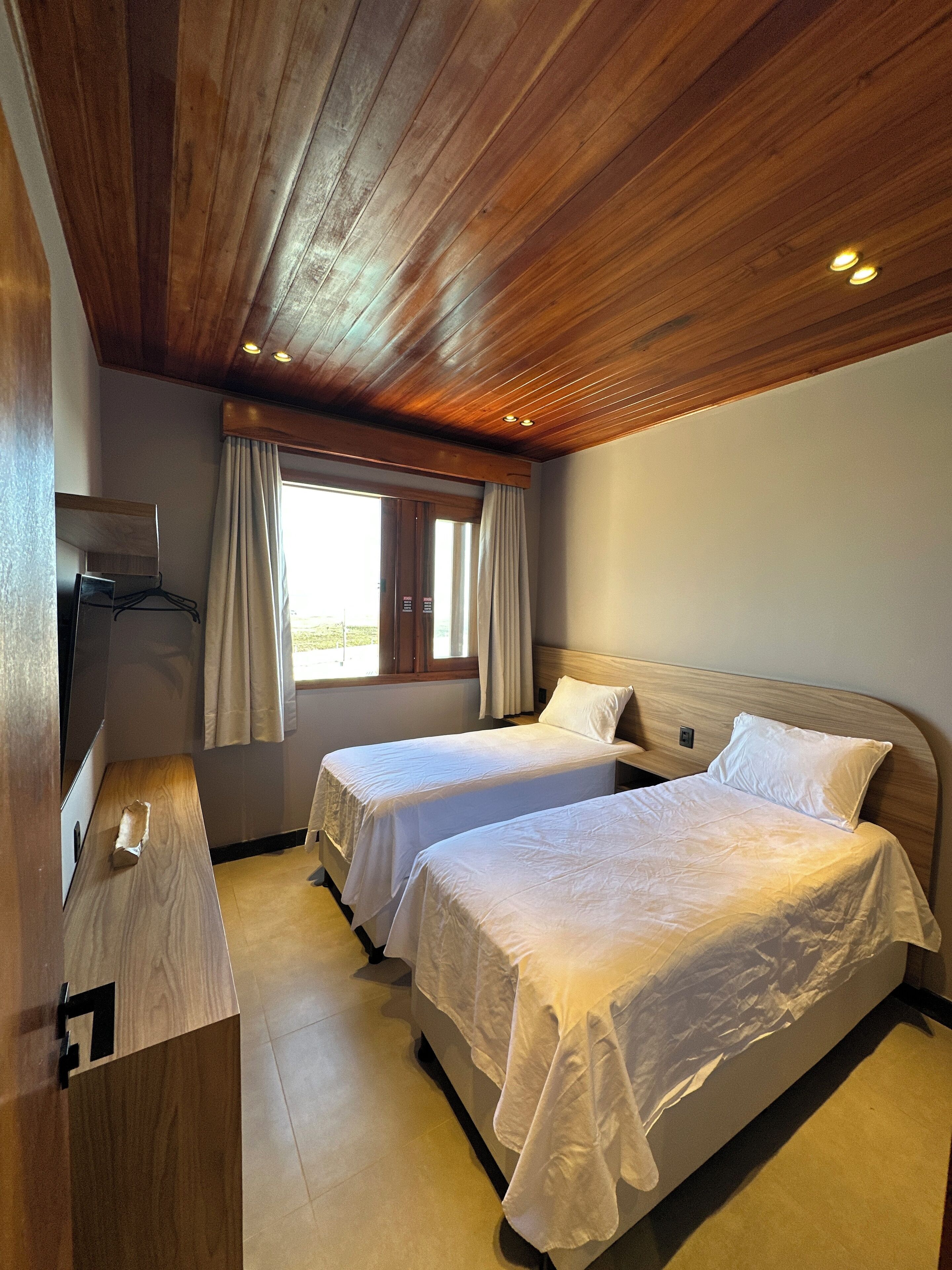 Habitación con dos camas, techo de madera y una ventana con cortinas.