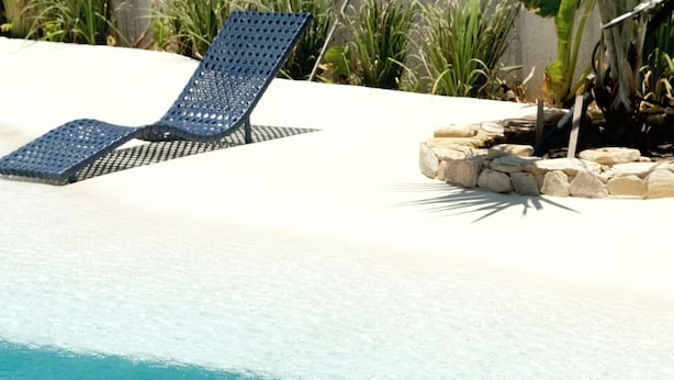 Una piscina con agua azul cristalina, una silla de descanso y un borde de piedra.