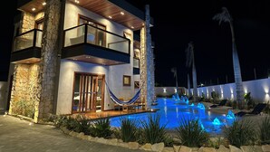 Una casa moderna de dos pisos con piscina, paredes de piedra y una hamaca.