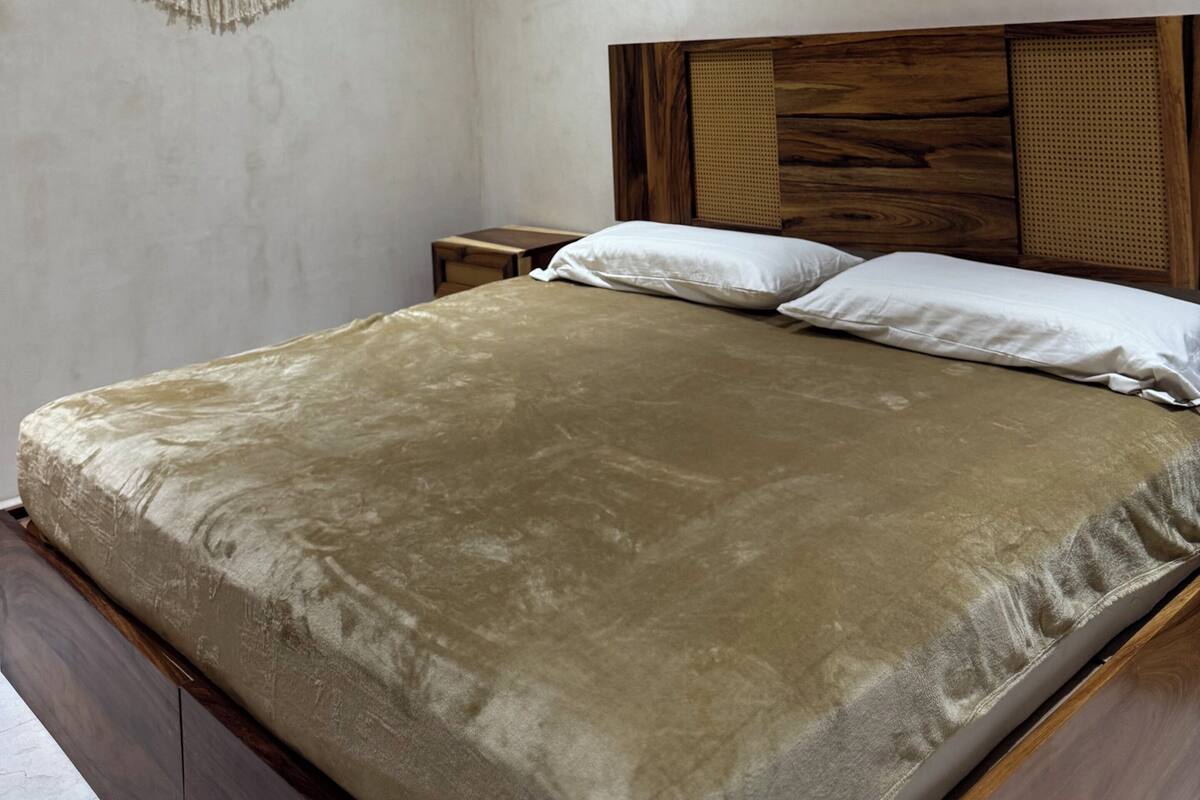 Een slaapkamer met een houten hoofdbord, een beige wand, een airconditioner, een nachtkastje en een hangende macramé wanddecoratie.