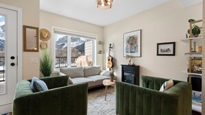 A cozy living room with a sofa, two green armchairs, a small coffee table, and a guitar.