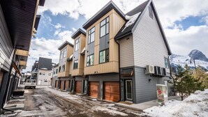 A row of modern multi-story buildings with large windows and garage doors, set against a snowy mountain backdrop.