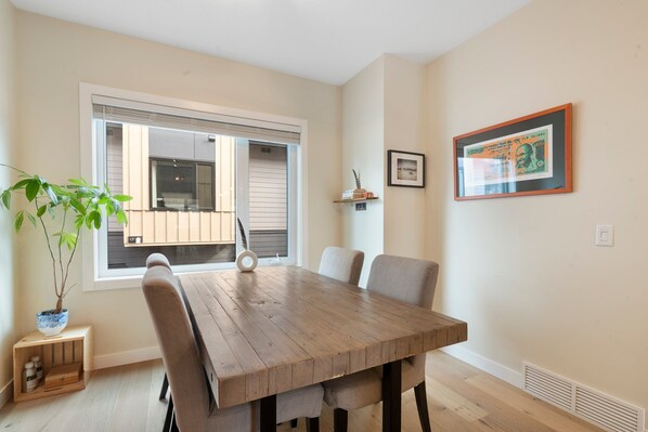 A dining area with a wooden table, four chairs, a potted plant, and a window with blinds. - Amazing Views, 10 Min to Downtown Canmore (Canmore)