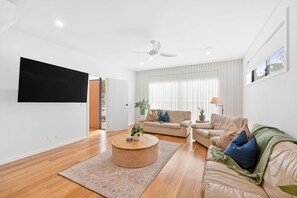 A modern living room with a flat-screen TV, a ceiling fan, and a large window with curtains.