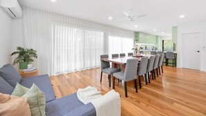 A modern living room with a sofa, dining table, and chairs, a kitchen area with cabinets, and a ceiling fan.