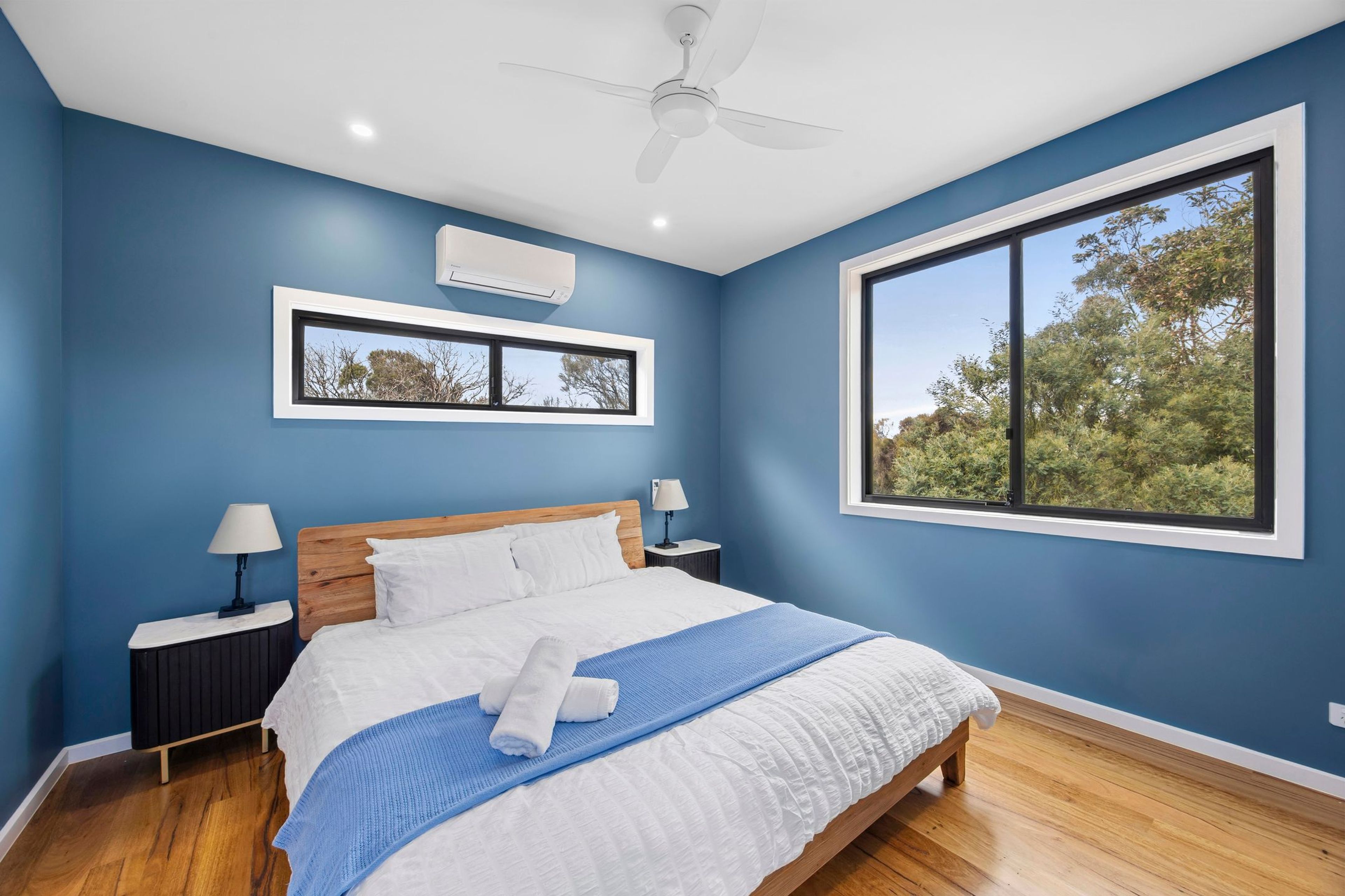 A bedroom with a large window, a ceiling fan, and a bed with white bedding.