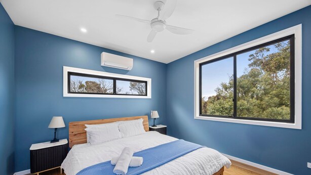 A bedroom with a large window, a ceiling fan, and a bed with white bedding.