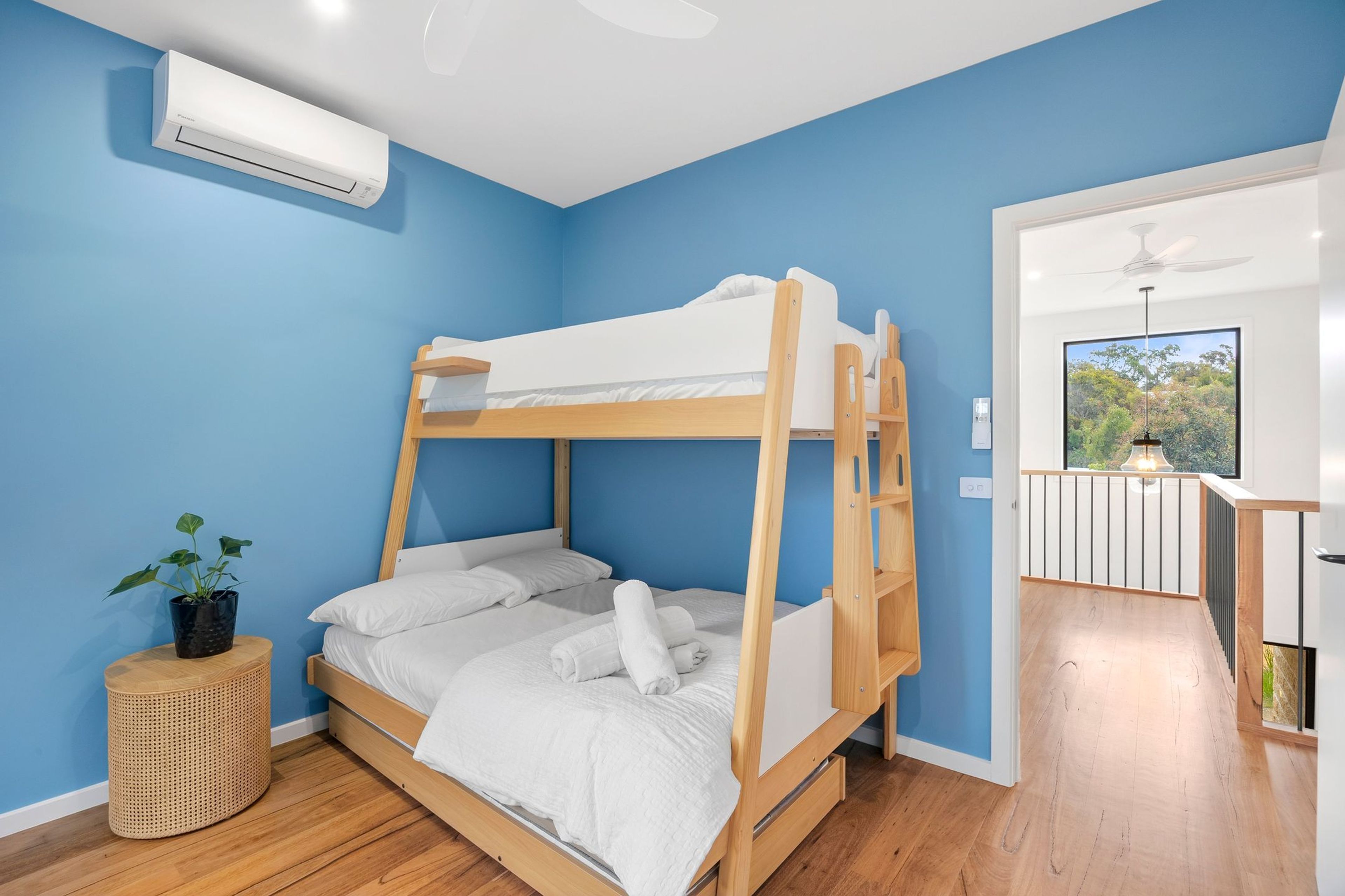 A bunk bed room with a ceiling fan, a potted plant, and a view of the outdoors through a window.