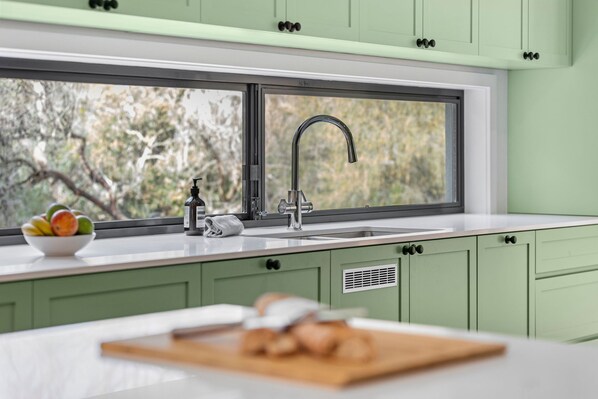A kitchen with a large window, a sink, and a bowl of fruit on the counter.