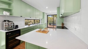 A modern kitchen with green cabinets, a white countertop, and a view to the outside.