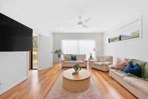 A modern living room with a flat-screen TV, two sofas, a coffee table, and a ceiling fan. - Gully & Tide (Aireys Inlet)