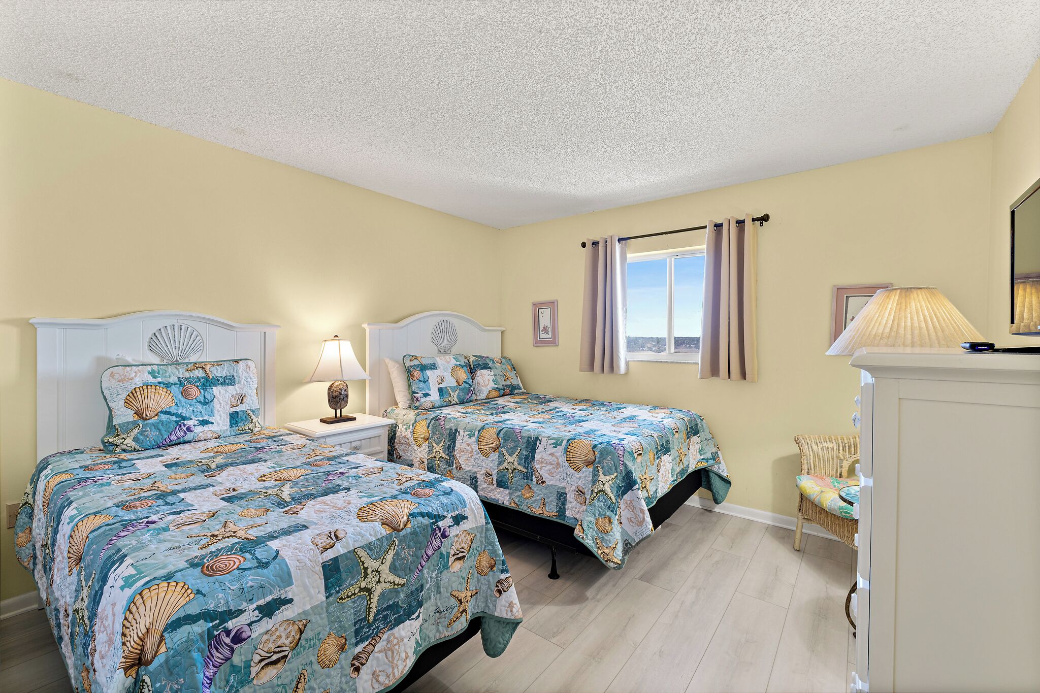 A bedroom with two beds, a nightstand, a lamp, a chair, and a window with curtains.