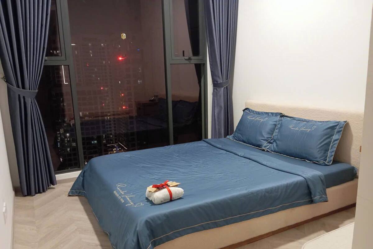 Ein Schlafzimmer mit Bett, einem Fenster mit Vorhängen und Blick auf die Stadt bei Nacht.