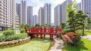 A red bridge over a pond in a park with tall residential buildings in the background. - Rose Vinhomes (Ho Chi Minh City)