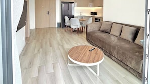 A modern living room with a brown sofa, a round coffee table, and a dining area with chairs and a table. - Rose Vinhomes (Ho Chi Minh City)