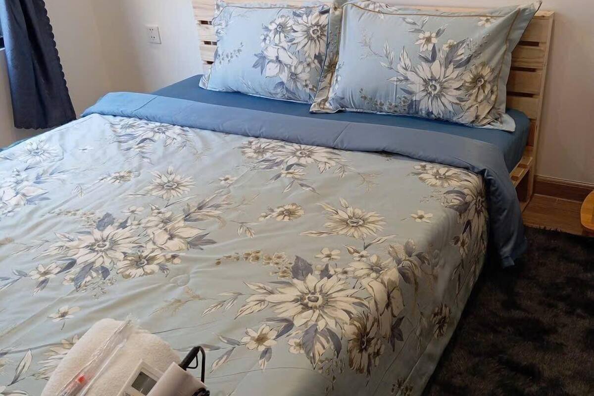 Ein Bett mit blumigem Bettbezug, ein Korb mit Pflegeprodukten und ein hölzernes Kopfteil.