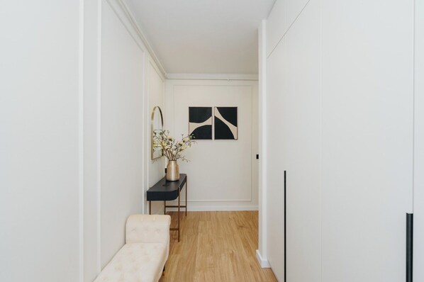 A hallway with a bench, a console table with a vase of flowers, and two abstract wall art pieces.