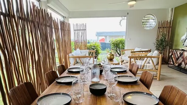 A dining table set for 8 with chairs, a vase of flowers, and a view of the outdoors. - SAINTE LUCE A STONE'S THROW FROM THE BEACH (Sainte-Luce)