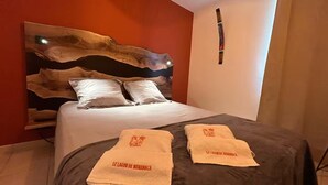 A bed with a wooden headboard, white pillows, and two towels with text. - SAINTE LUCE A STONE'S THROW FROM THE BEACH (Sainte-Luce)