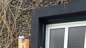 A wooden sign with "ANEX" and "AL" on it, a white door with a glass panel, and a stone wall with some vegetation. - Charming 1-bedroom apartment in amazing Angra do Heroísmo with WiFi (Angra do Heroísmo)