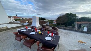 An outdoor dining area with a table set for four, surrounded by chairs, on a rooftop with a view of the sea and buildings in the background. - Charming 1-bedroom apartment in amazing Angra do Heroísmo with WiFi (Angra do Heroísmo)