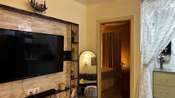 Una sala de estar con una gran televisión de pantalla plana, un espejo decorativo, una estantería y una puerta que da a otra habitación.