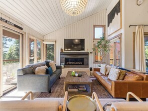 A spacious living room with a fireplace, large windows, and a view of the outdoors.