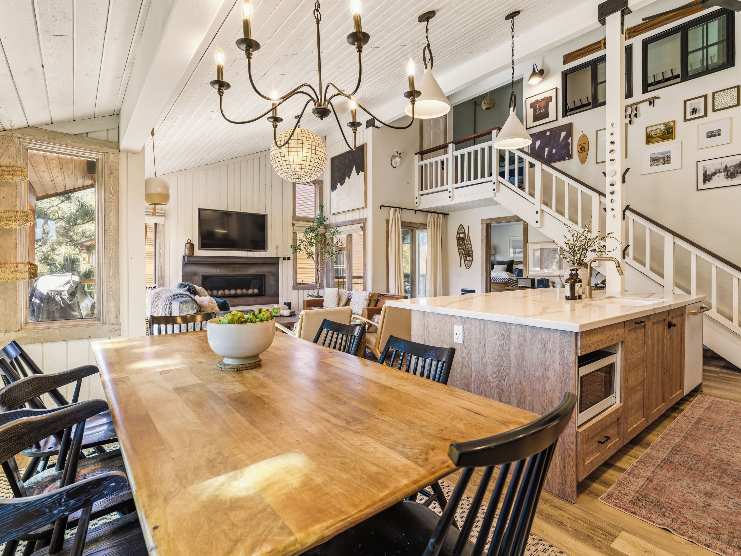 A spacious dining area with a wooden table and chairs, a large bowl of fruit, and a television above the fireplace.