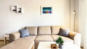 Uma sala de estar moderna com um sofá seccional bege, uma mesa de centro branca e uma obra de arte emoldurada acima do sofá.