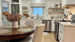 A modern kitchen with white cabinetry, stainless steel appliances, and a dining area with a round table and chairs. - The Driftwood, Saint Andrews (St. Andrews)